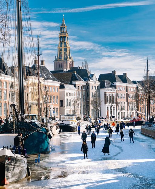People ice skating on the frozen canals of Groningen, Netherlands, with the Martinitoren tower in the background