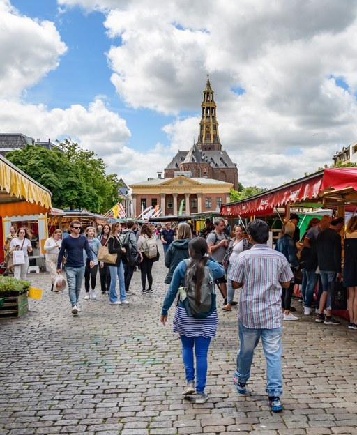 The Groningen Vismarkt fish market on a sunny day, with colourful market stalls and the historic Der A-a Kerk church rising in the background