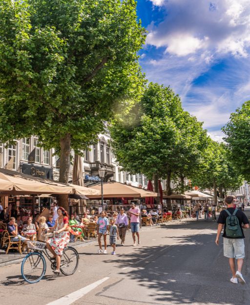 The Vrijthof square in Maastricht on a busy summer day, with cafe terraces and green trees lining the cobblestones