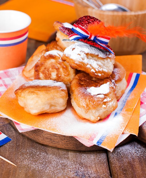 A plate of fresh Dutch oliebollen dusted with icing sugar, decorated with orange Dutch colours