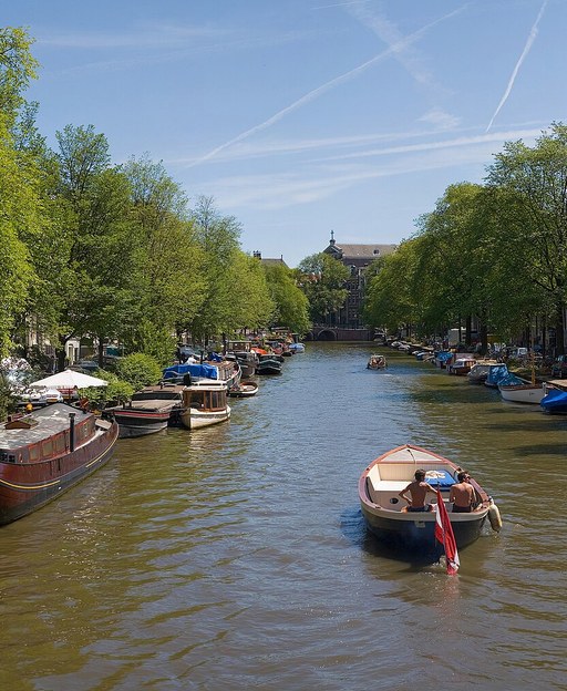 Serene tree-lined Amsterdam canal receding into the distance with boats, Netherlands