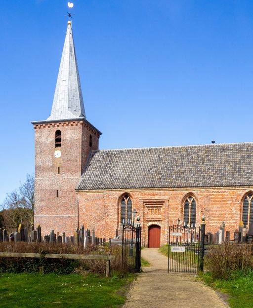 An old church in a Friesland village in the Netherlands, surrounded by flat green fields and sky
