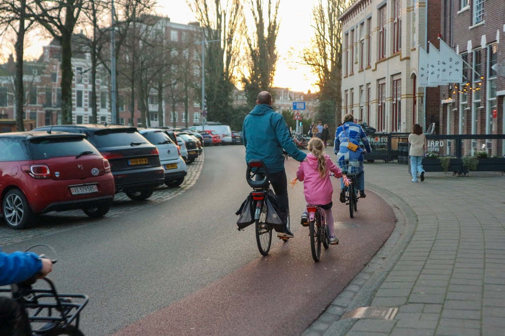 Adult and children cycling together on a tree-lined street in a Dutch town