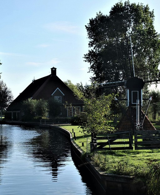 A traditional Dutch farmhouse with a small windmill beside clear water in Friesland, the Netherlands