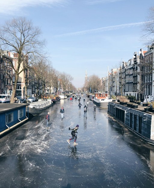 Skaters gliding across a frozen Amsterdam canal lined with houseboats and canal houses