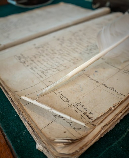 Old handwritten ledger pages with a feather quill resting on them
